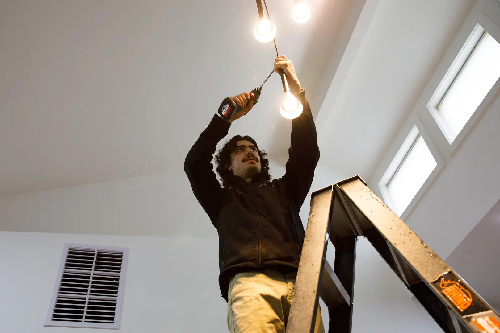 Person fixing ceiling lights with power drill.
