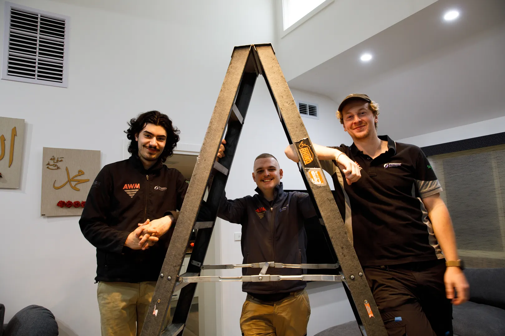 Three men smiling around a ladder indoors.